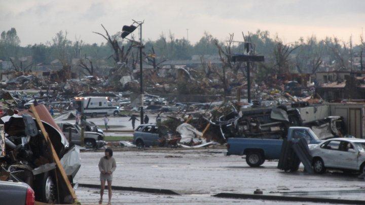 People outside, looking at the damaged neighborhood. No undamaged buildings visible.